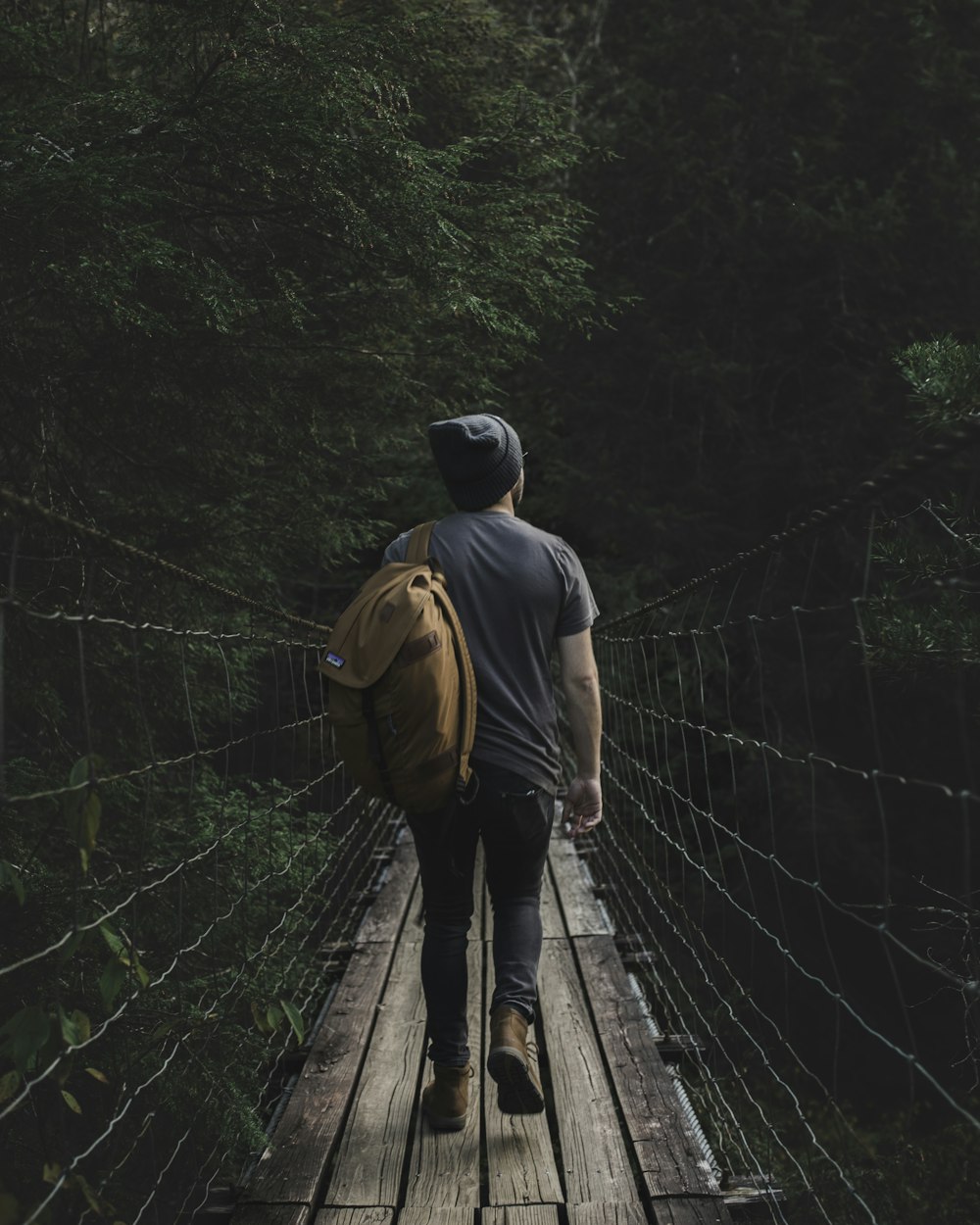 a man walking across a suspension bridge in the woods