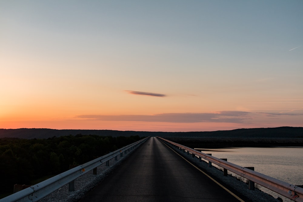 the sun is setting over the water on the road