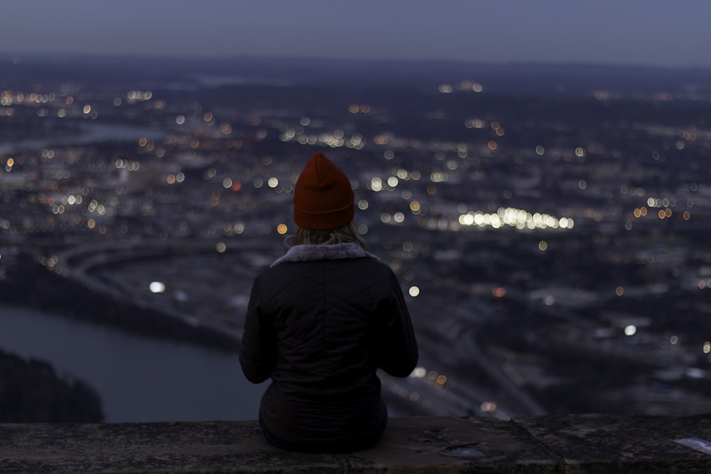 una persona seduta su una sporgenza che domina una città di notte