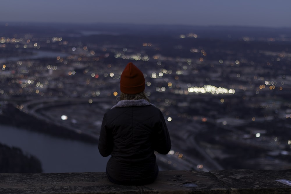 a person sitting on a ledge overlooking a city at night