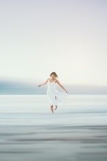 a woman in a white dress jumping in the air