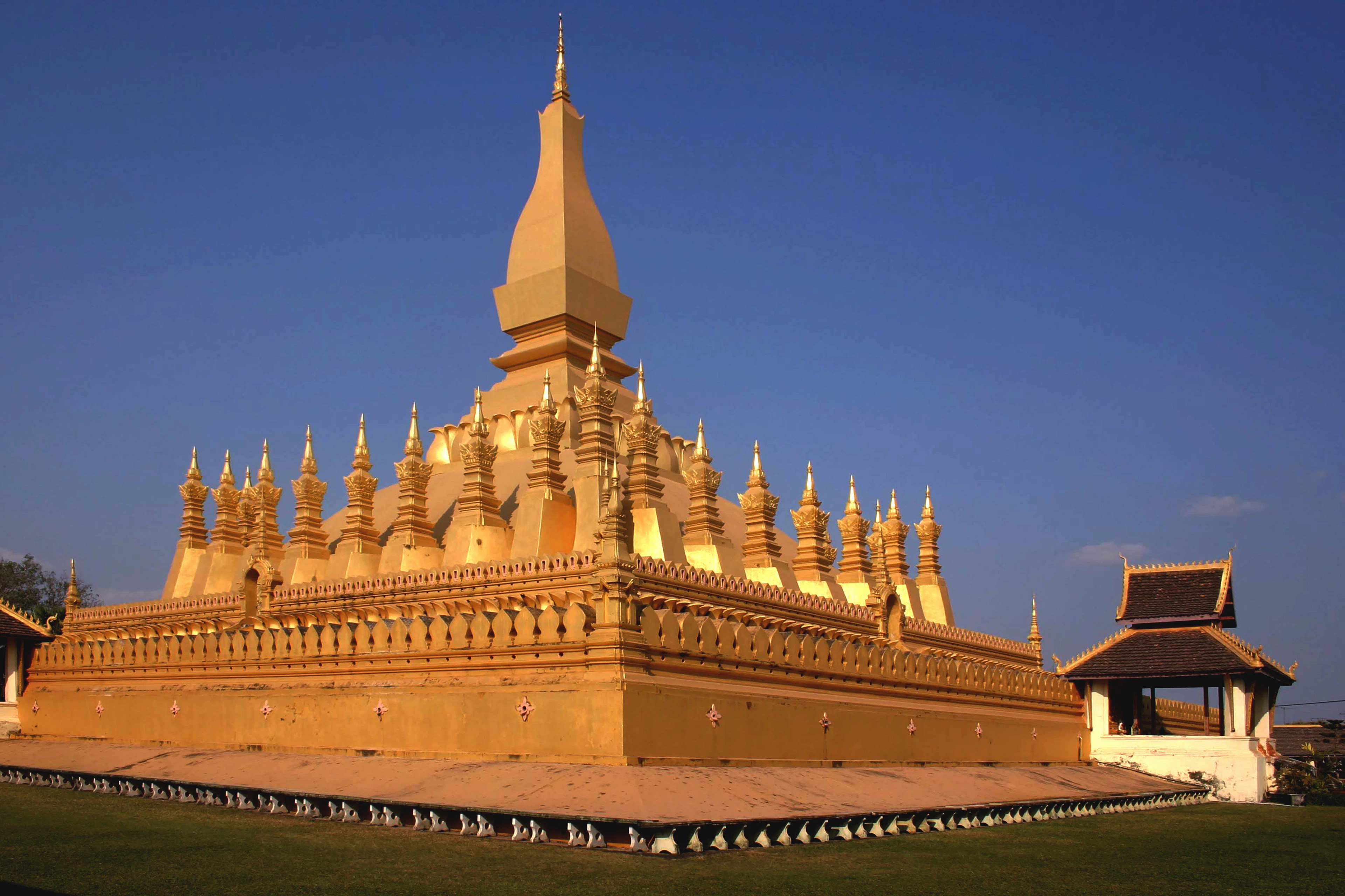 The gilded central stupa and spired cloister of Pha That Luang glowing gold under a deep blue sky in Vientiane, Laos