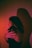 A person with long hair is embracing themselves with their arms wrapped around their shoulders. The light casts a dramatic shadow on the wall, creating an intriguing and introspective visual. The lighting features a blend of pink and red hues, adding a warm and intimate atmosphere.