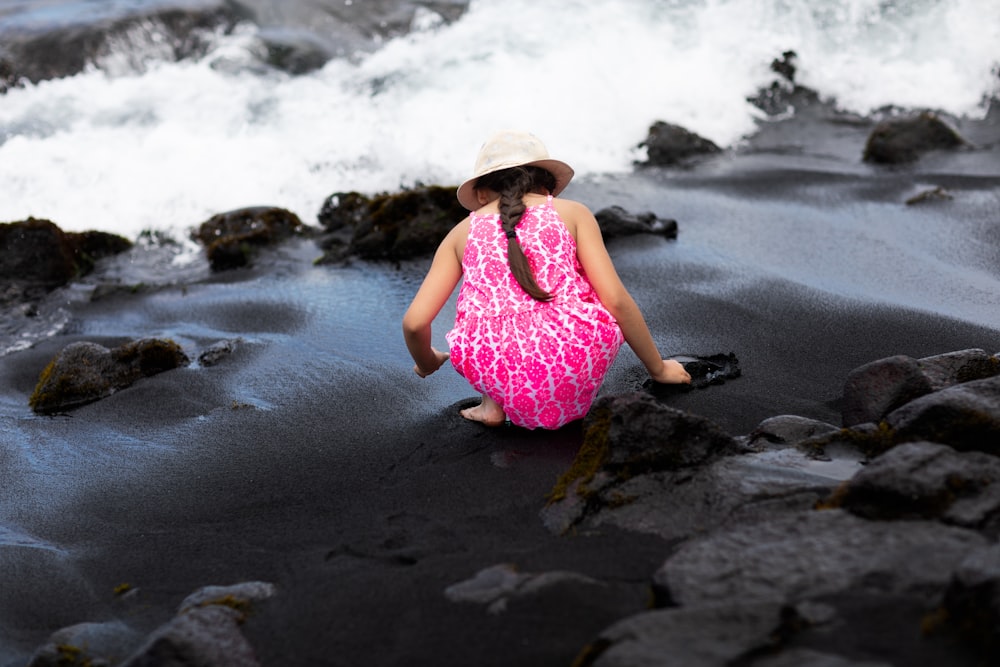 Una niña con un vestido rosa sentada en una playa negra