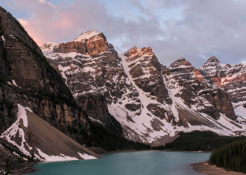 a lake surrounded by snow covered mountains under a cloudy sky