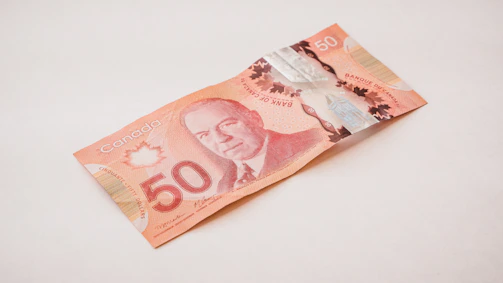 Artistic composition of a Canadian dollar bill resting on a wooden table with soft natural light.