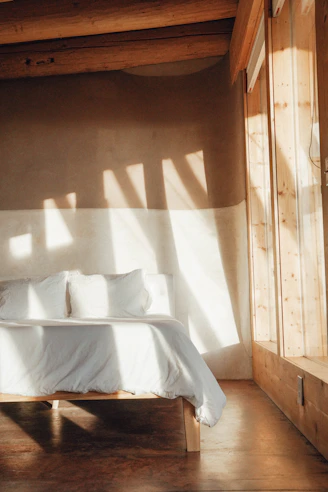 A cozy bedroom featuring a solid wood bed frame with an upholstered tufted headboard bathed in warm natural light.