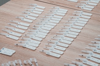 Numerous white rapid test kits are arranged in neat rows on a wooden surface. Each kit appears to have numbers or labels marked on them, likely for identification purposes.