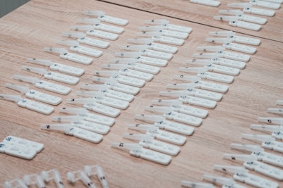 Numerous white rapid test kits are arranged in neat rows on a wooden surface. Each kit appears to have numbers or labels marked on them, likely for identification purposes.