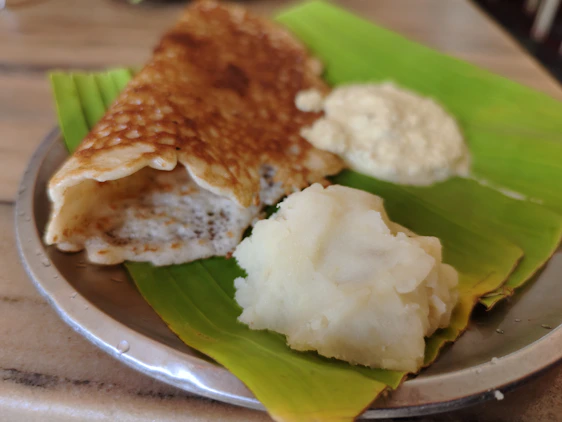 Fresh golden Madras dosa on a traditional banana leaf with chutneys and sambar in rustic South Indian setting.
