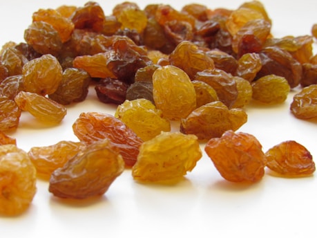 Clusters of sun-kissed raisins glistening on a simple white plate with a backdrop of earthy tones.