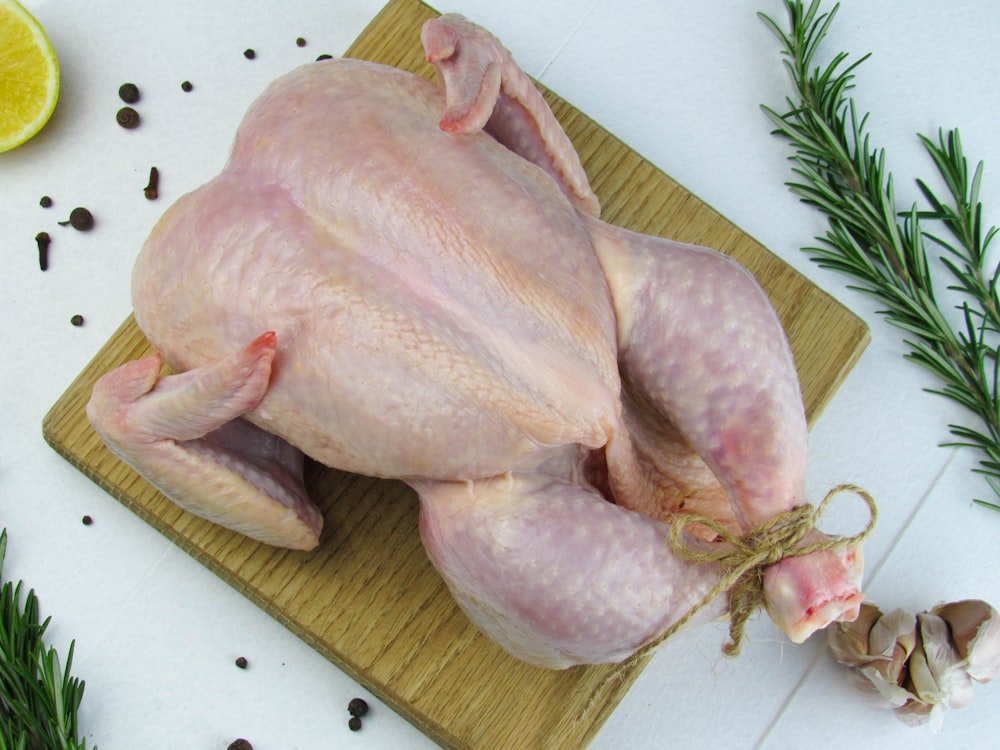 a raw chicken on a cutting board next to a slice of lemon