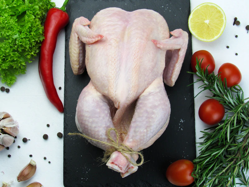 Whole raw chicken on a dark board with chillies, garlic and tomatoes