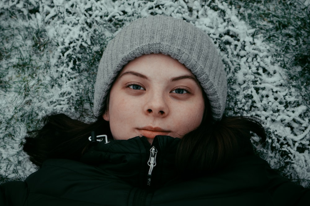 a woman laying in the snow wearing a hat