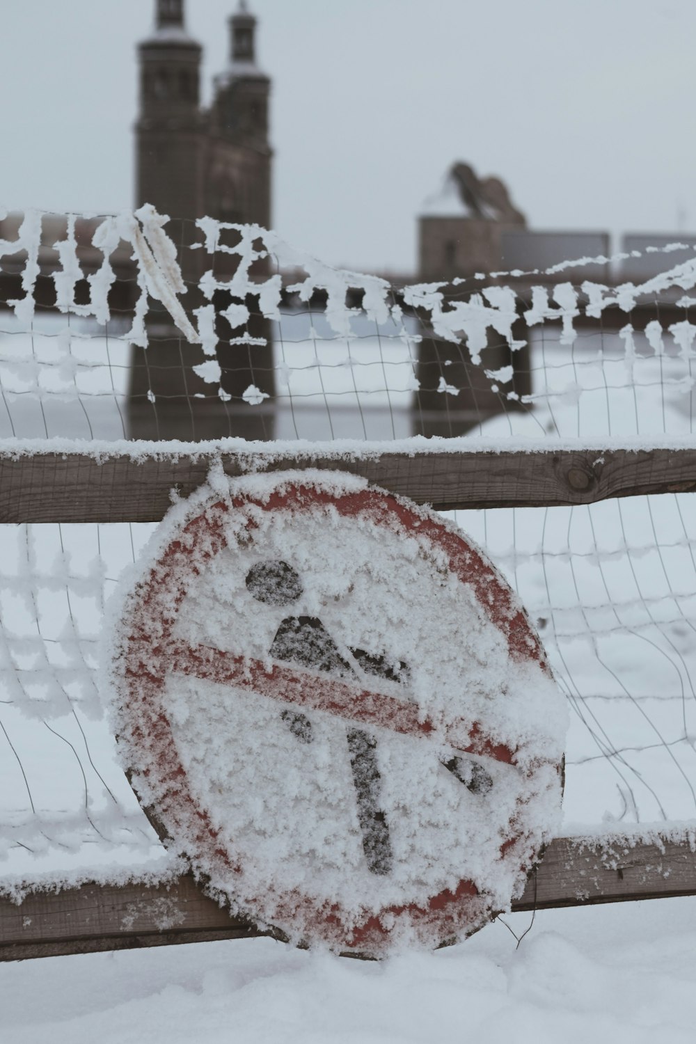 a no parking sign covered in snow in front of a fence