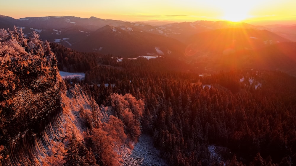 the sun is setting over the mountains and trees