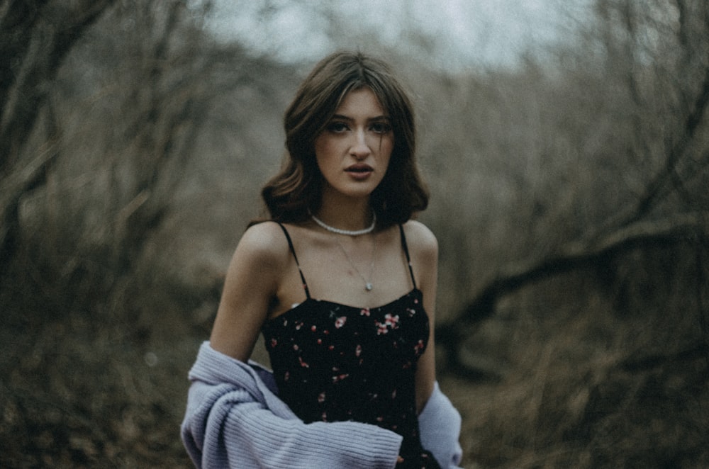 a woman in a black dress standing in a forest