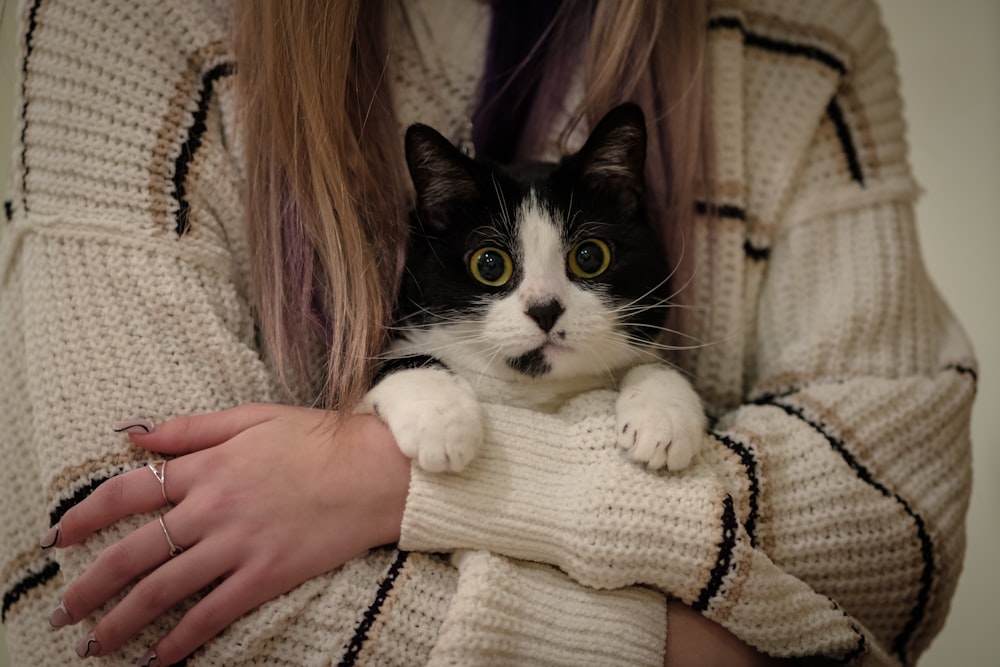a woman holding a black and white cat in her arms
