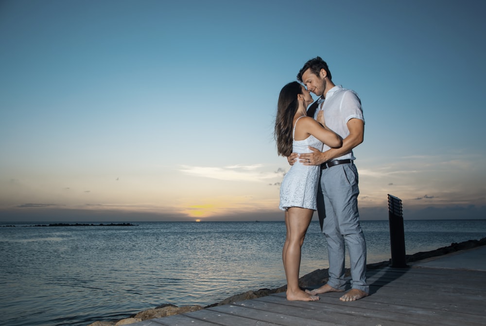 a man and woman standing on a dock next to the ocean