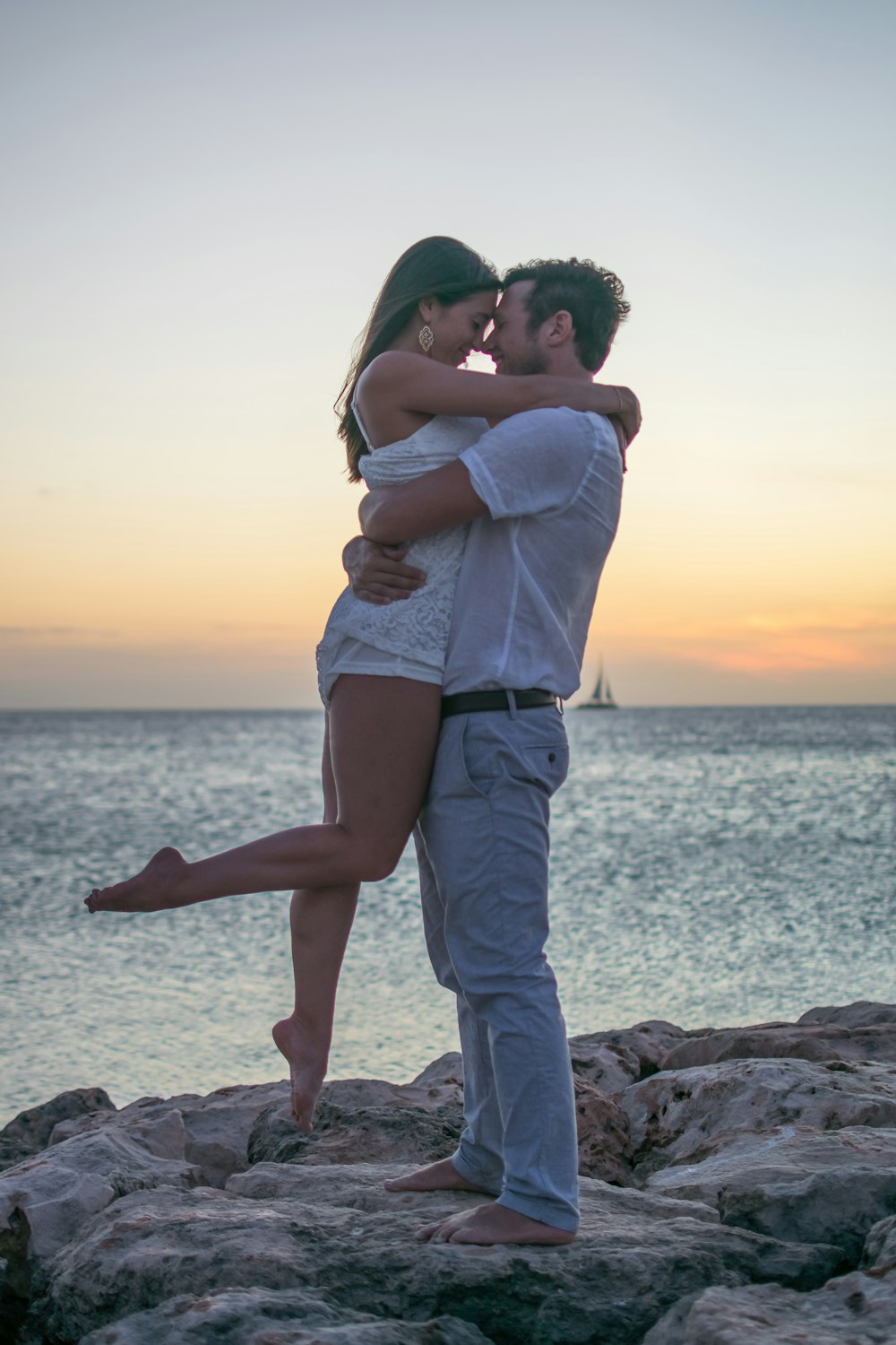 a man and a woman standing on a rock near the ocean