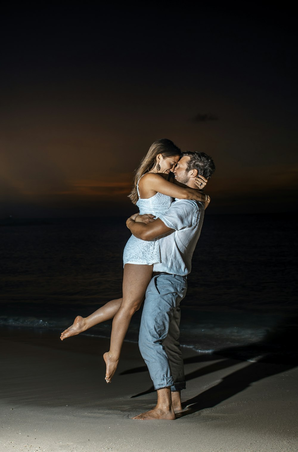 a man and woman embracing on the beach at night