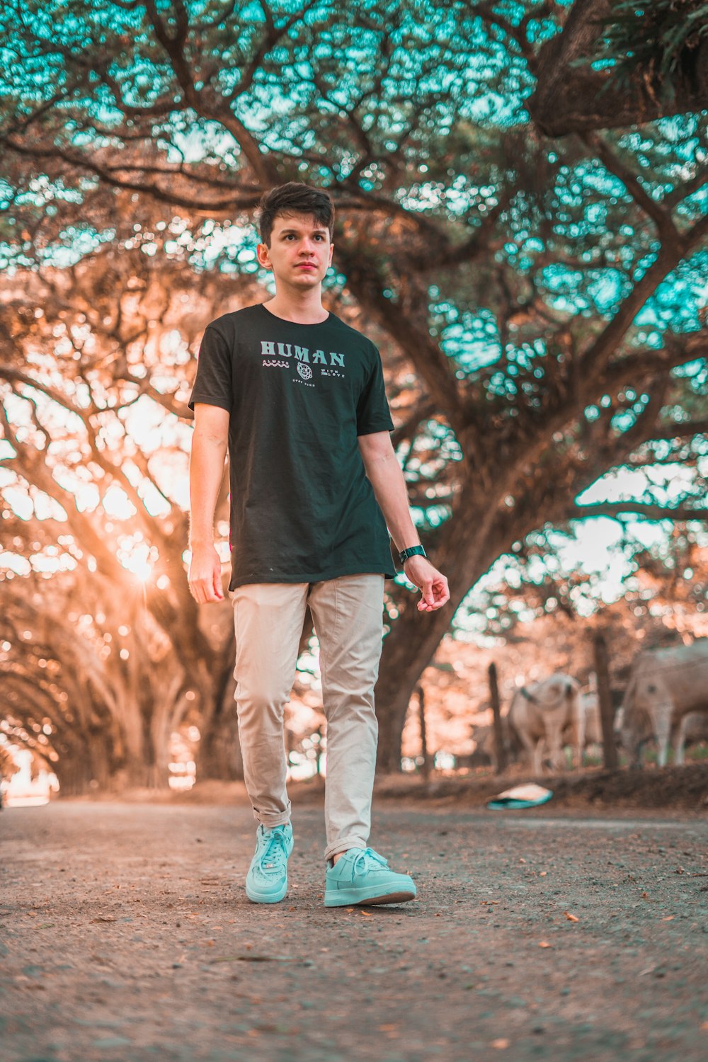 a man walking down a dirt road with trees in the background