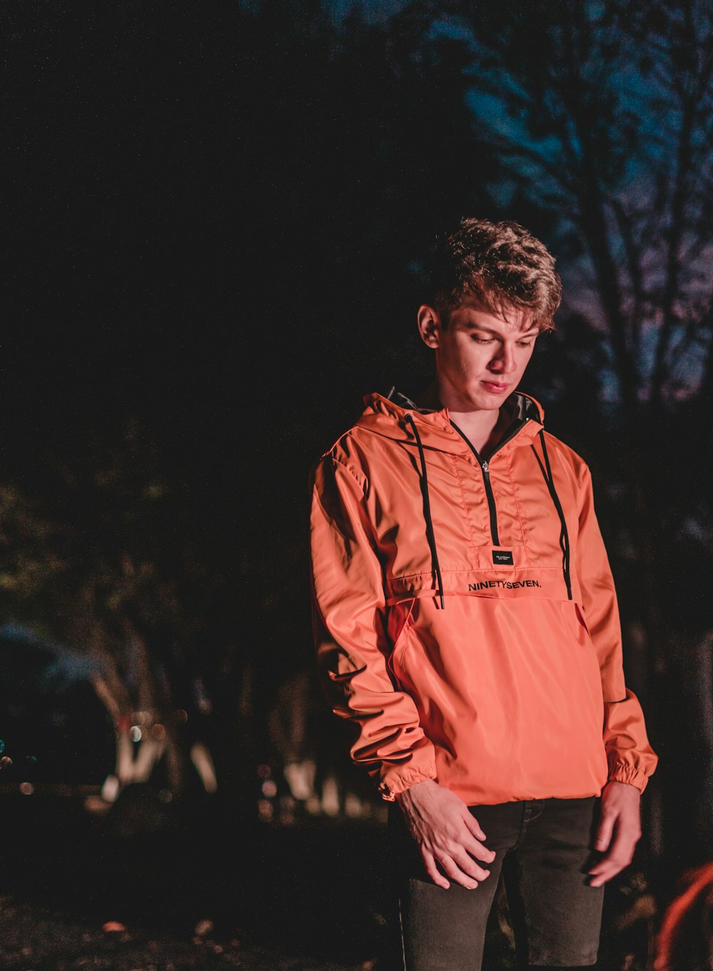 オレンジ色のパーカーを着て暗闇の中に立つ若い男