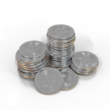 A collection of silver-colored coins stacked in piles, each coin bearing a Bitcoin symbol. The coins are arranged on a white surface, creating a reflective and metallic effect.