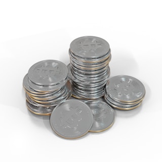A collection of silver-colored coins stacked in piles, each coin bearing a Bitcoin symbol. The coins are arranged on a white surface, creating a reflective and metallic effect.