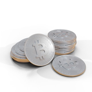 A pile of shiny silver coins decorated with a prominent Bitcoin symbol on the surface. Each coin is meticulously detailed, with engraved text encircling the central logo, indicating a digital currency motif.