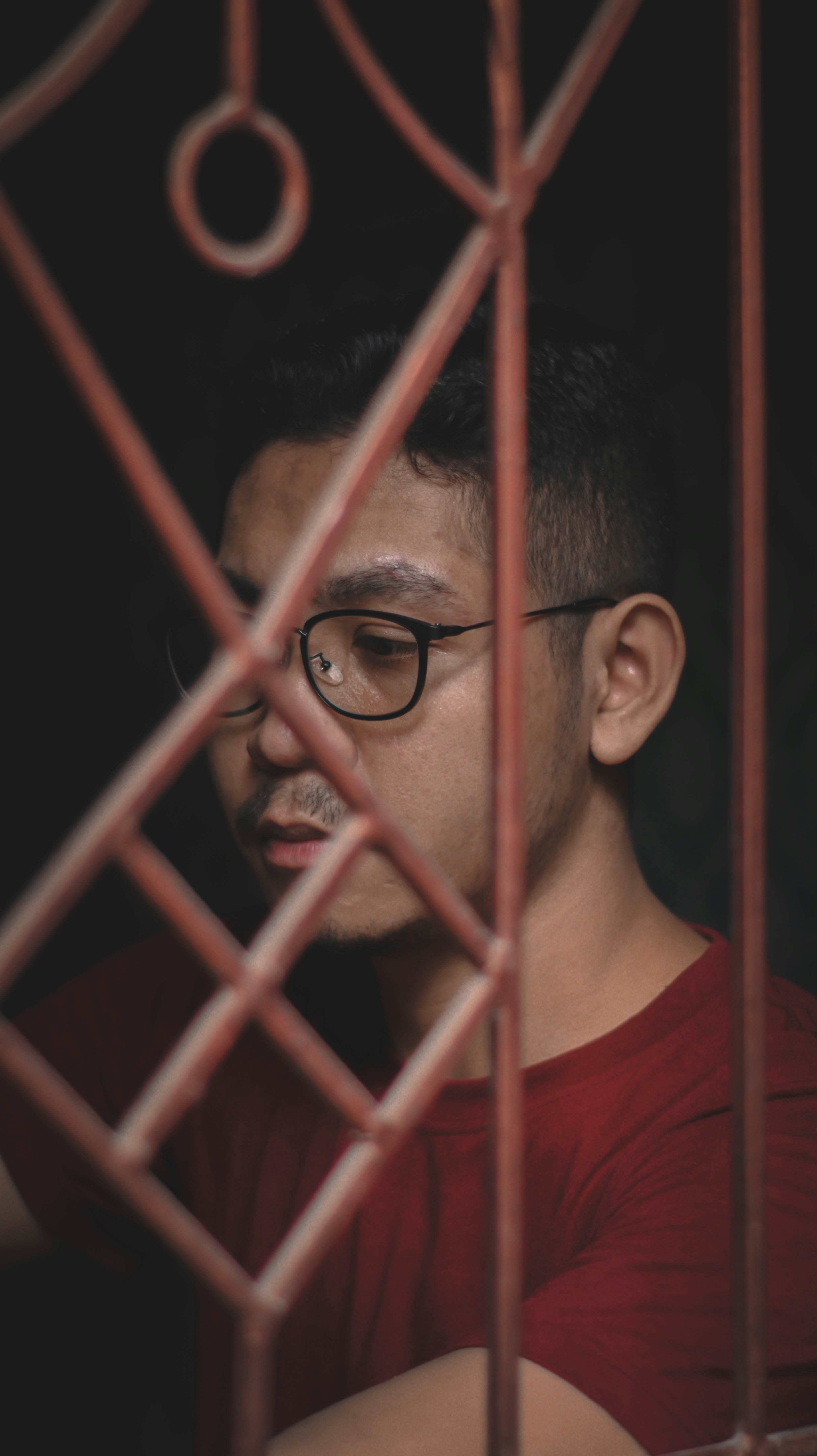 a man wearing glasses looking through a red fence