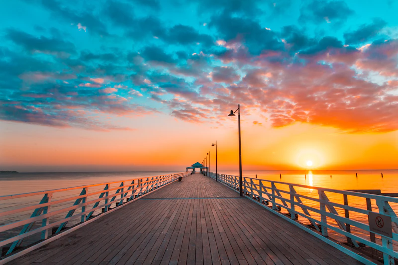 A timber jetty reaching into the ocean beneath a golden sunset