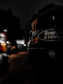A close-up of a black helmet with the brand name 'STUDDS' prominently displayed. The background is a city street at night, blurred with bokeh lights, suggesting an urban environment. The lighting is dim, focusing on the reflective surface of the helmet.
