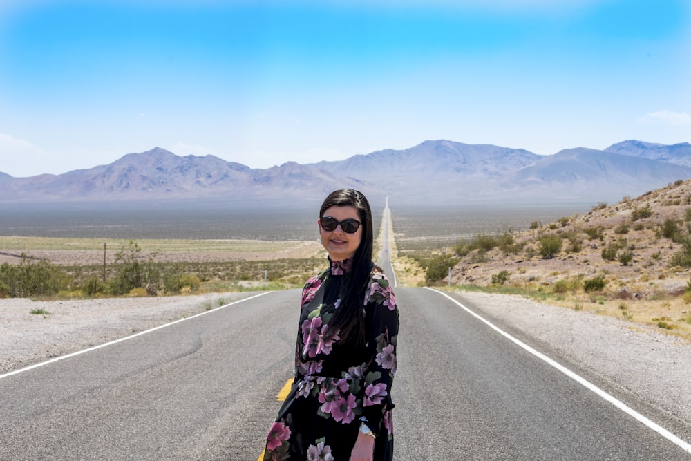 a woman standing on the side of a road with mountains in the background