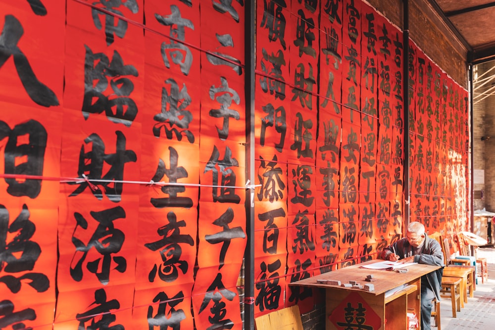 a man sitting at a desk in front of a red wall