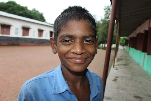 A smiling teenager receiving guidance from a mentor outdoors, with a backdrop of community activity.