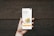 A hand holding a smartphone in front of a wooden background. The phone screen displays a financial investment application with the text 'The smartest thing to do with your money'. Below it, there are illustrations of stacked coins and a call-to-action button labeled 'Start investing'.