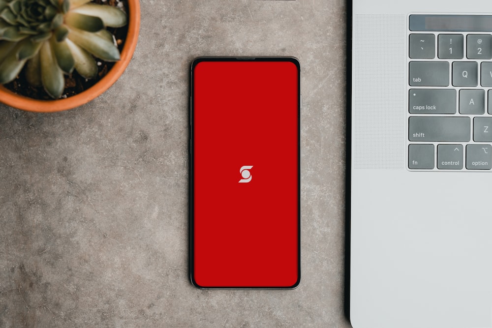 Un teléfono celular rojo sentado junto a una computadora portátil