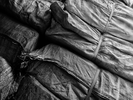 Tightly packed and stacked burlap sacks with visible textures and patterns of the fabric, held together by straps.