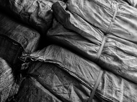 Tightly packed and stacked burlap sacks with visible textures and patterns of the fabric, held together by straps.