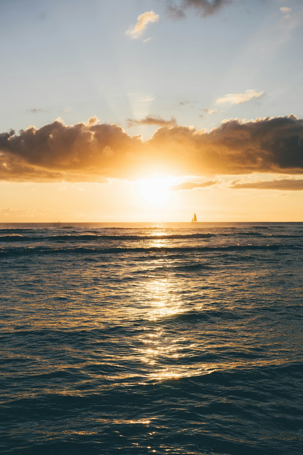 the sun is setting over the ocean with a sailboat in the distance