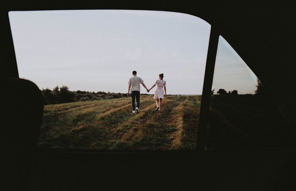 a man and a woman holding hands walking across a field