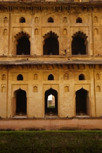 A historical building facade with intricate arched windows and doorways, displaying a blend of decorative stonework and architectural design. The structure appears aged, with a weathered and rustic texture on the walls. Light and shadows play across the surfaces, highlighting the detailed craftsmanship.