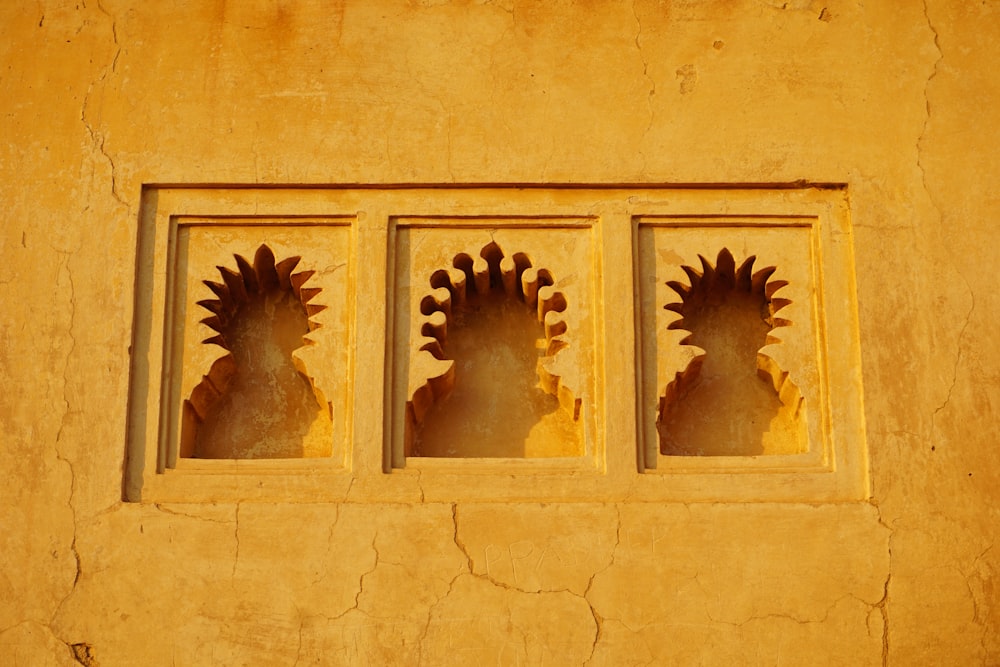 Tres ventanas con diseños decorativos en una pared amarilla