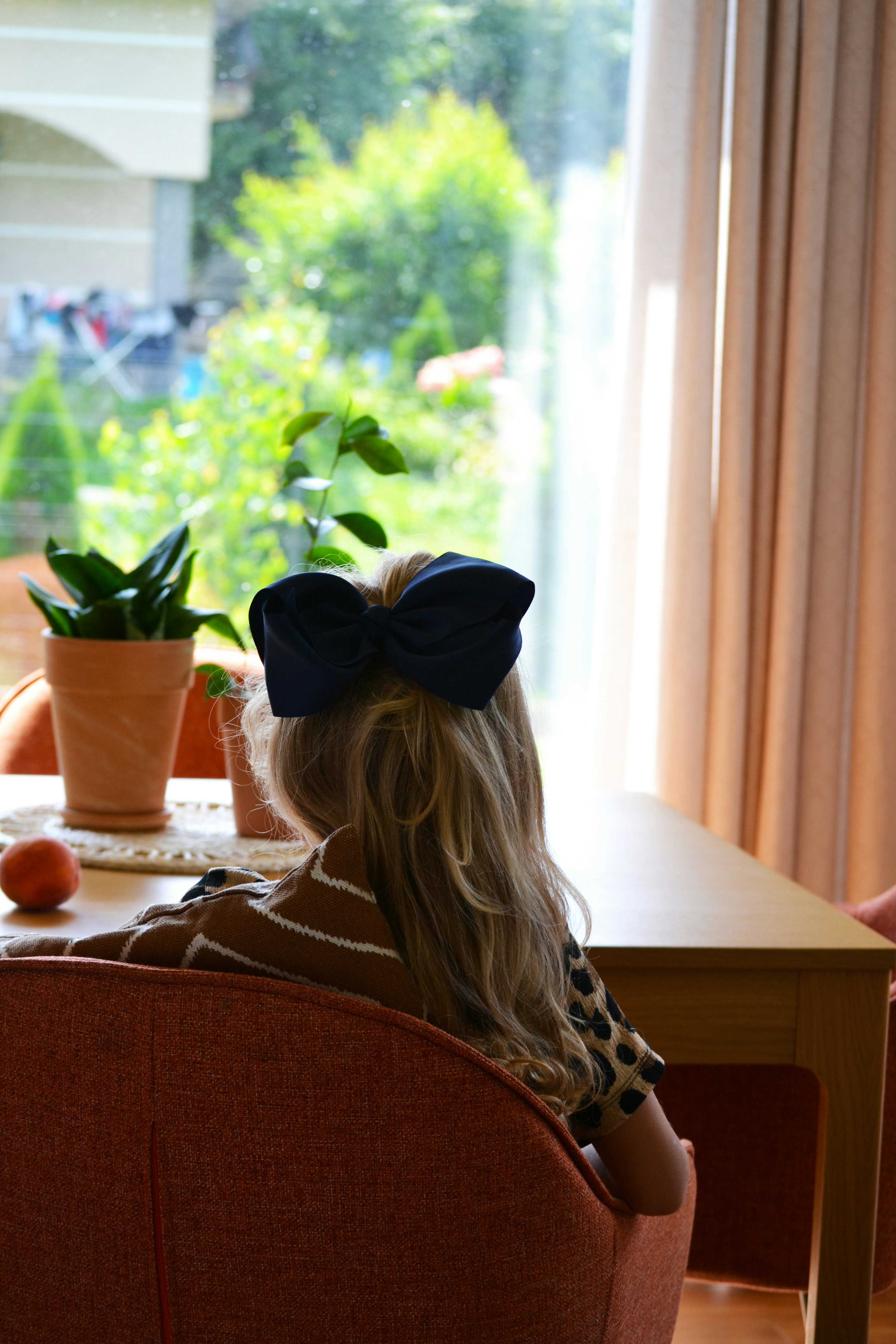 a little girl sitting in a chair looking out a window