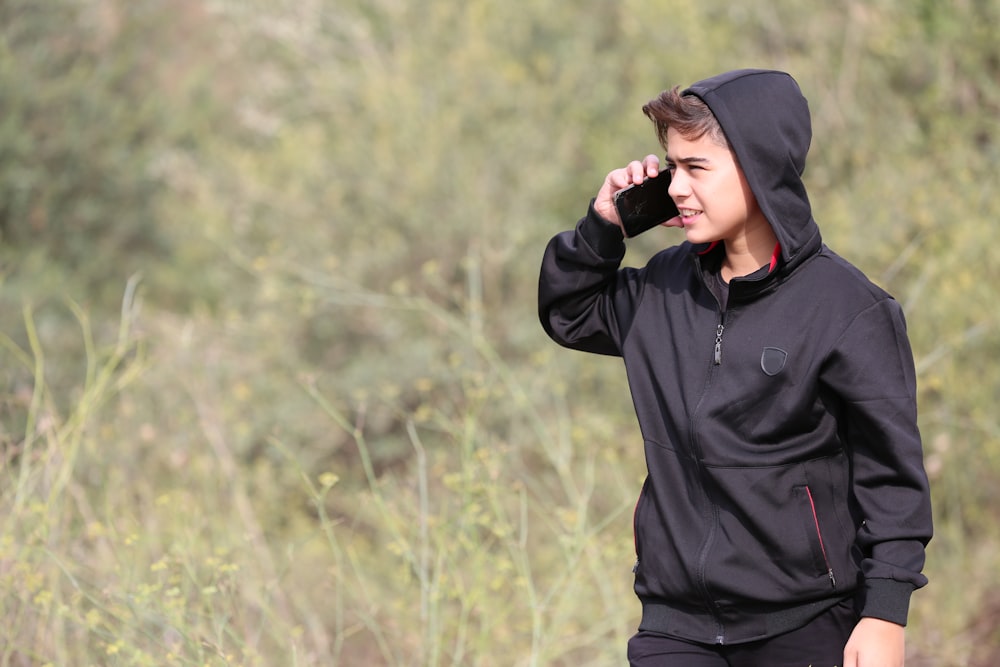 a boy in a black hoodie talking on a cell phone