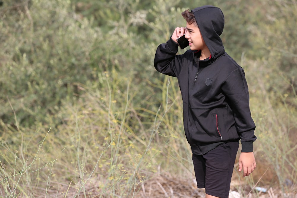 a young man in a black hoodie talking on a cell phone