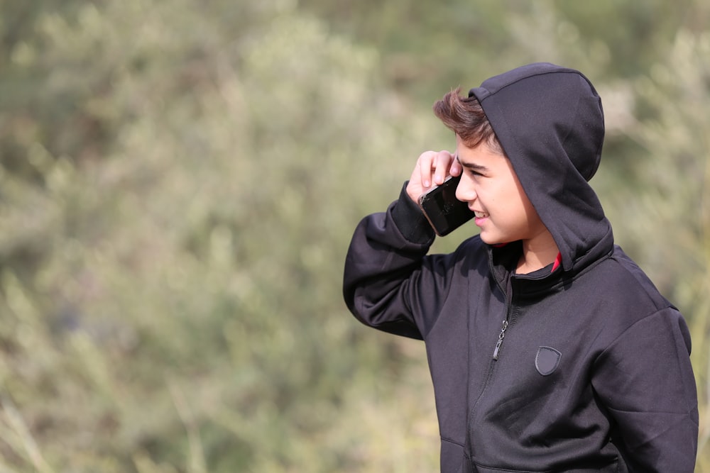 a young boy in a black hoodie talking on a cell phone