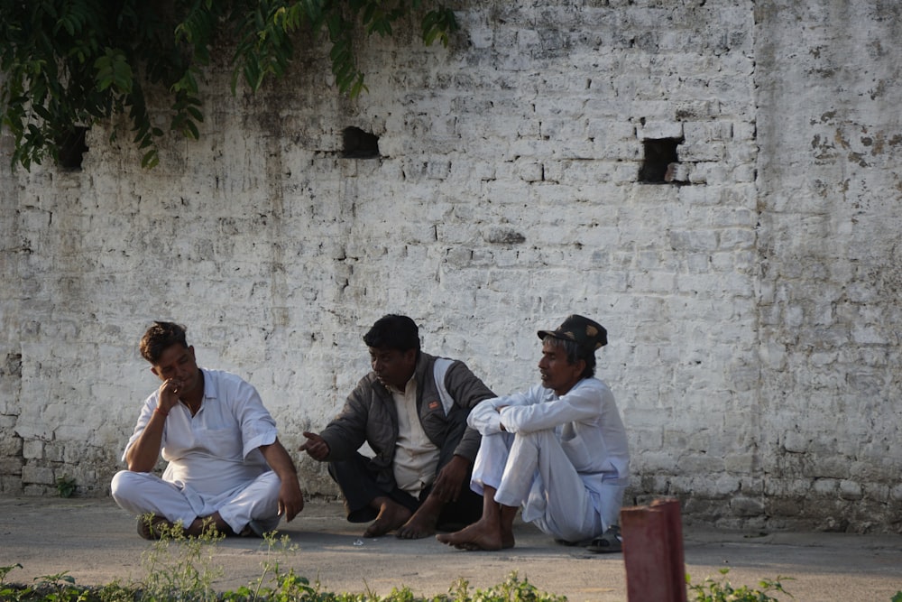 three people sitting on the ground near a brick wall