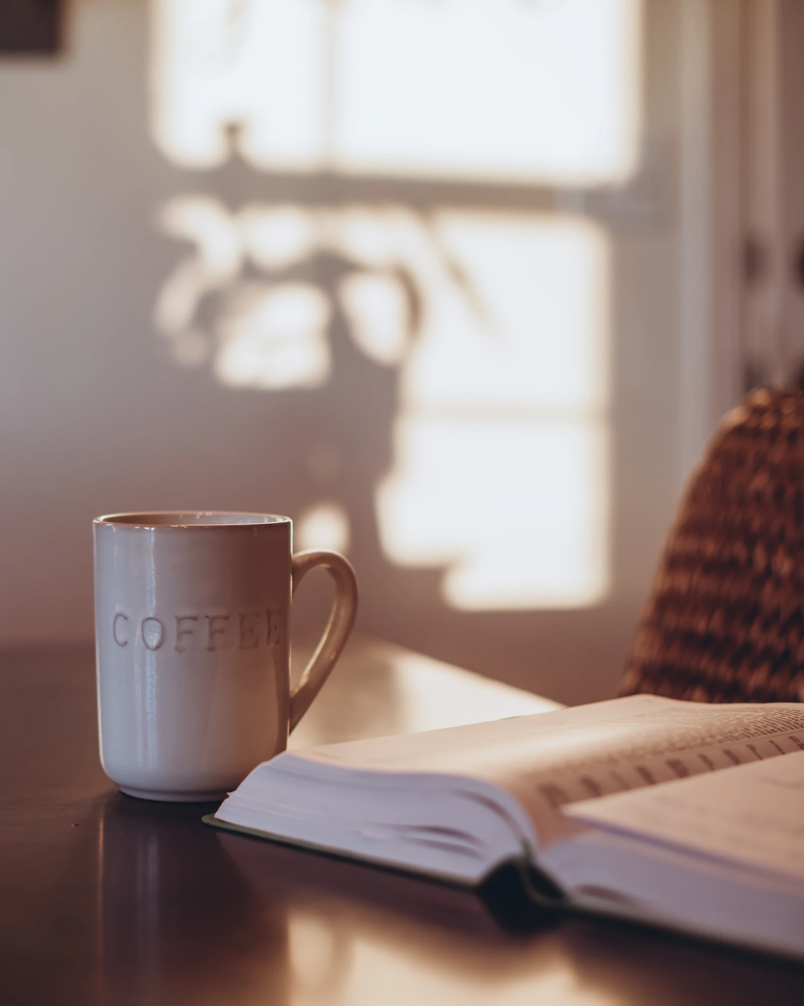 A coffee mug on a table next to an open book in warm natural light